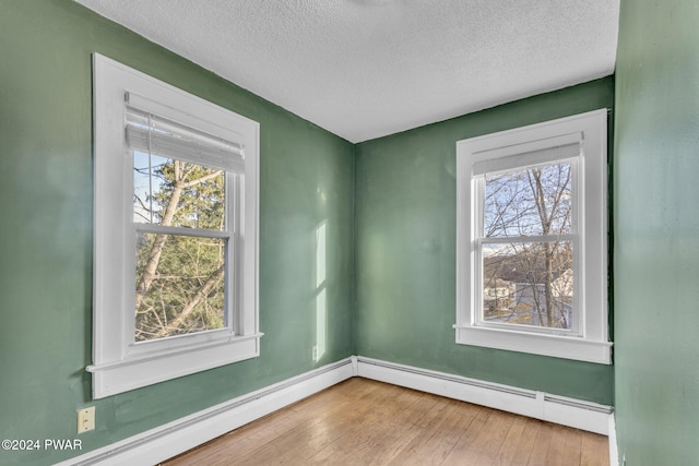 spare room featuring baseboard heating, a wealth of natural light, and hardwood / wood-style flooring