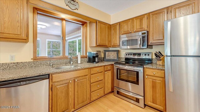 kitchen with stainless steel appliances, a sink, light wood finished floors, and light stone counters