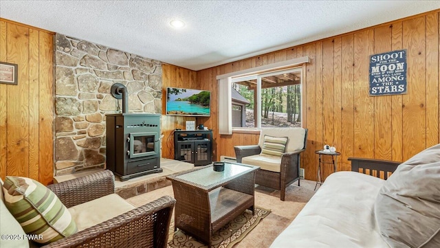 carpeted living room with a textured ceiling, wood walls, a wood stove, and a baseboard heating unit