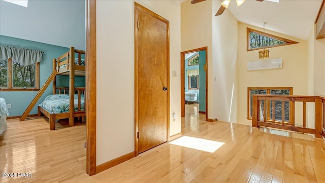 hallway with light wood-style floors, high vaulted ceiling, and baseboards