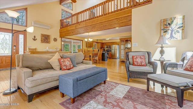 living area with light wood finished floors, a chandelier, a wall mounted air conditioner, and a towering ceiling