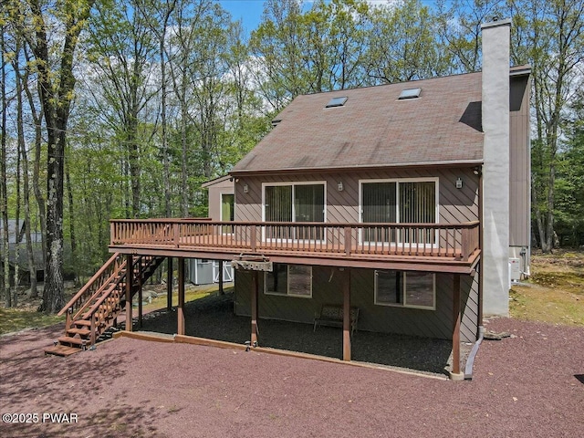 rear view of house with a deck, a chimney, stairway, and a shingled roof