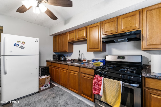 kitchen with gas range, white refrigerator, dark stone countertops, and sink