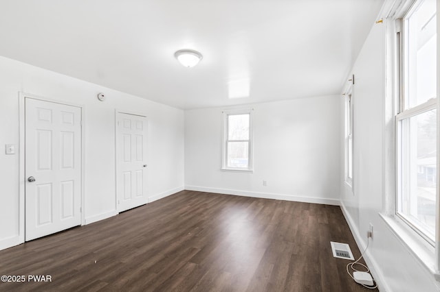 empty room featuring a wealth of natural light and dark wood-type flooring