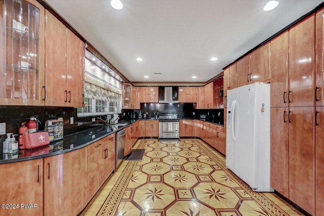 kitchen with tasteful backsplash, wall chimney exhaust hood, stainless steel appliances, sink, and dark stone countertops