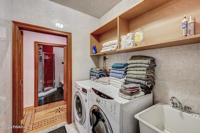 laundry area with washer and clothes dryer, sink, and tile walls