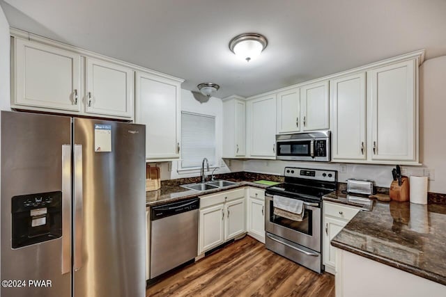 kitchen featuring appliances with stainless steel finishes, dark wood-type flooring, sink, dark stone countertops, and white cabinetry