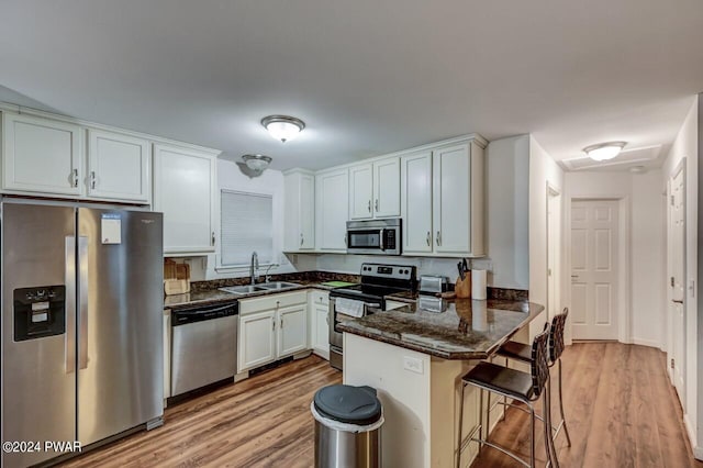 kitchen with kitchen peninsula, appliances with stainless steel finishes, a breakfast bar, sink, and white cabinetry