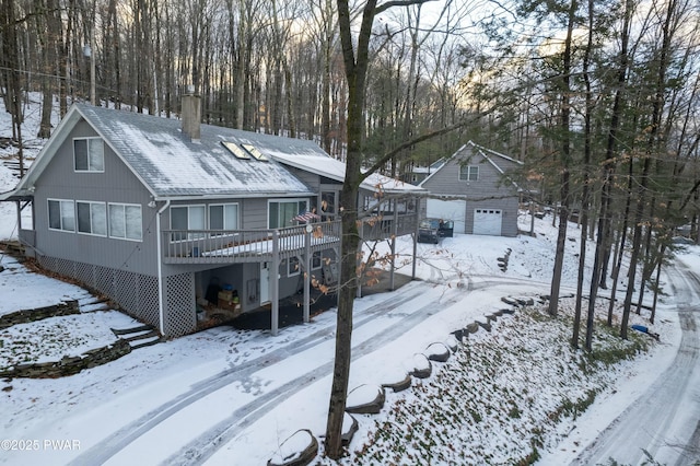 snow covered rear of property with a wooden deck and an outdoor structure