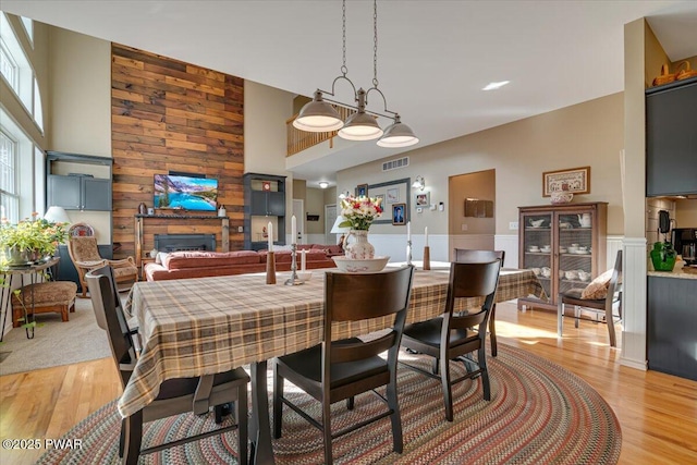 dining area with light wood finished floors, visible vents, wood walls, and a fireplace