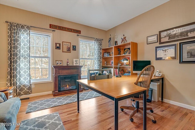 office area with a glass covered fireplace, wood finished floors, and baseboards