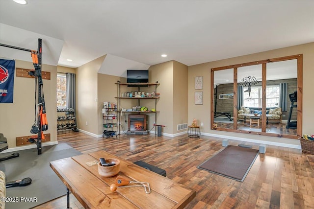 exercise room with wood finished floors, visible vents, baseboards, recessed lighting, and a lit fireplace