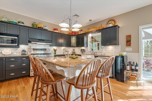 kitchen featuring a breakfast bar area, light stone countertops, stainless steel appliances, under cabinet range hood, and light wood-type flooring