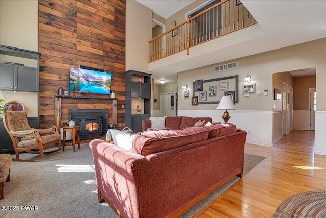 living area featuring a wainscoted wall, visible vents, light wood finished floors, a high ceiling, and a glass covered fireplace