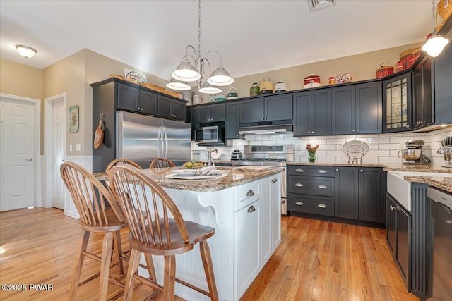 kitchen with under cabinet range hood, a breakfast bar area, light stone countertops, and appliances with stainless steel finishes