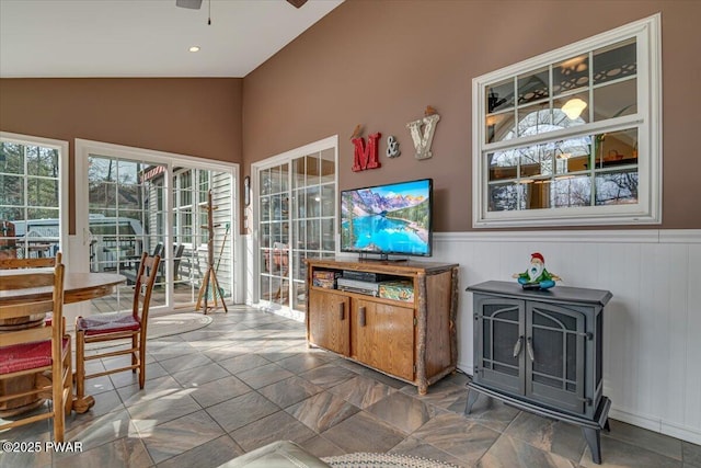 interior space featuring vaulted ceiling, a wood stove, a ceiling fan, and a wainscoted wall