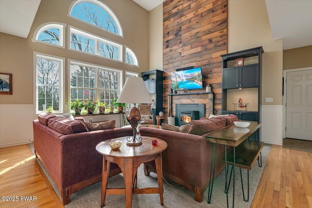 living area with a wainscoted wall, a large fireplace, light wood-style flooring, and a towering ceiling