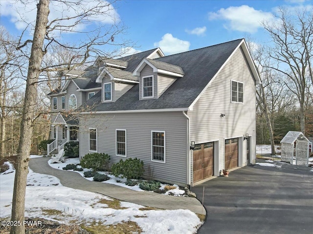 snow covered property with aphalt driveway, an attached garage, and roof with shingles