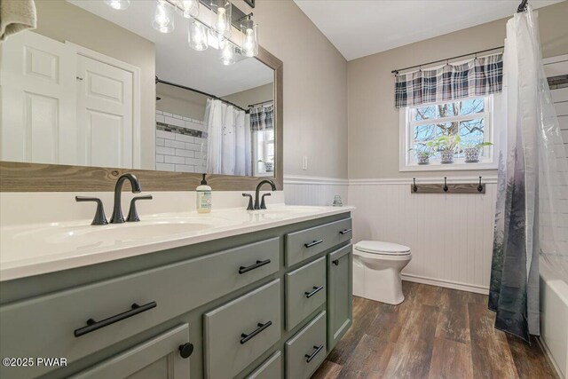 bathroom with toilet, wood finished floors, shower / bath combo with shower curtain, and wainscoting