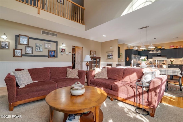 living room featuring a wainscoted wall, a high ceiling, and visible vents