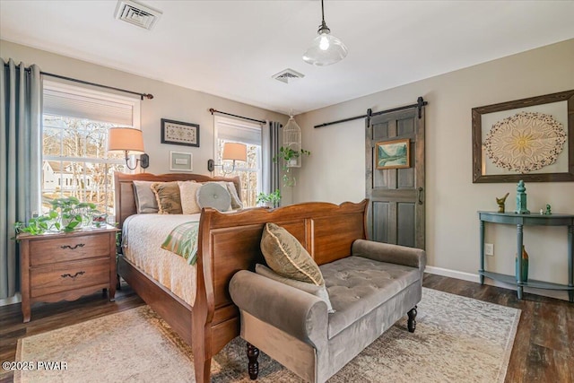 bedroom featuring visible vents, baseboards, a barn door, and wood finished floors