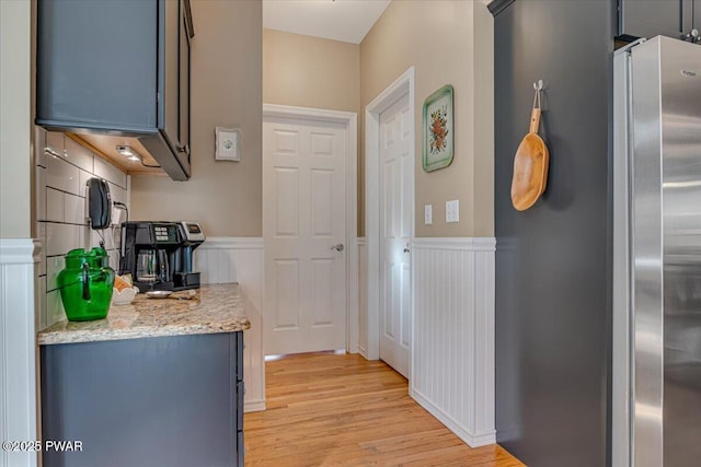 kitchen with light stone counters, a wainscoted wall, freestanding refrigerator, and light wood finished floors