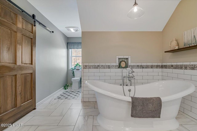 bathroom featuring a freestanding tub, toilet, tile walls, wainscoting, and lofted ceiling