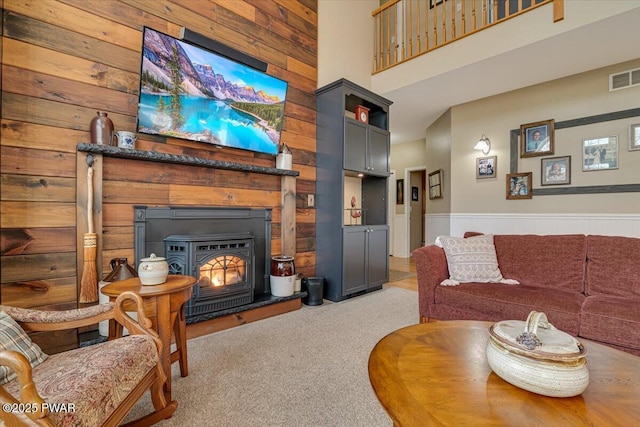 living area featuring visible vents, a wainscoted wall, carpet floors, wood walls, and a towering ceiling