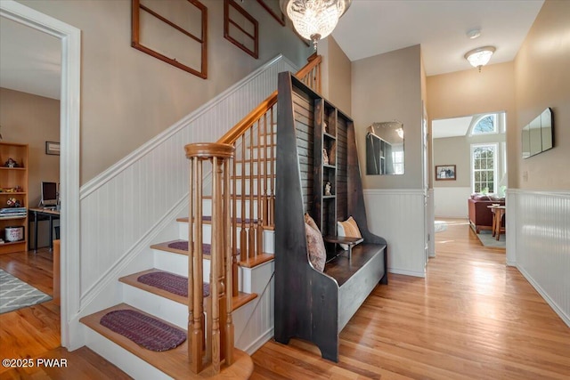 stairs featuring wood finished floors and a wainscoted wall