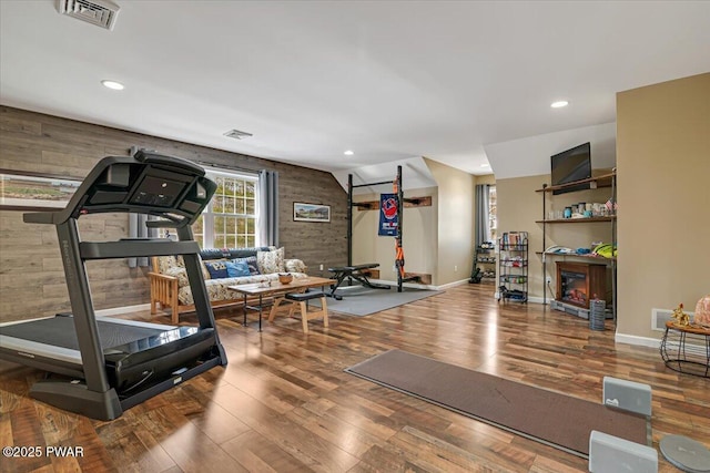 exercise room with visible vents, recessed lighting, wood-type flooring, and a glass covered fireplace