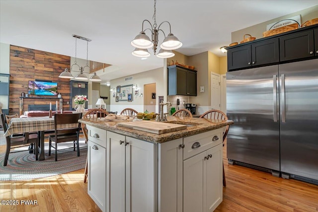 kitchen featuring a sink, light wood finished floors, stainless steel built in refrigerator, and wood walls