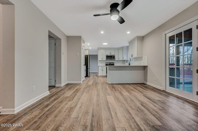 kitchen featuring light hardwood / wood-style flooring, stainless steel appliances, white cabinets, decorative backsplash, and kitchen peninsula