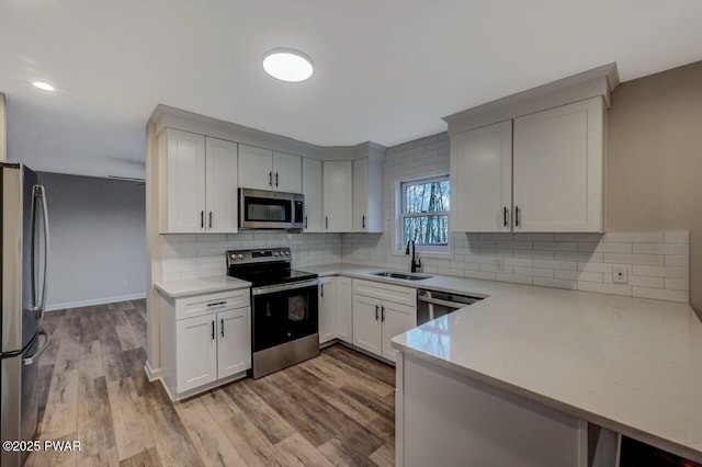 kitchen with sink, tasteful backsplash, appliances with stainless steel finishes, kitchen peninsula, and white cabinets