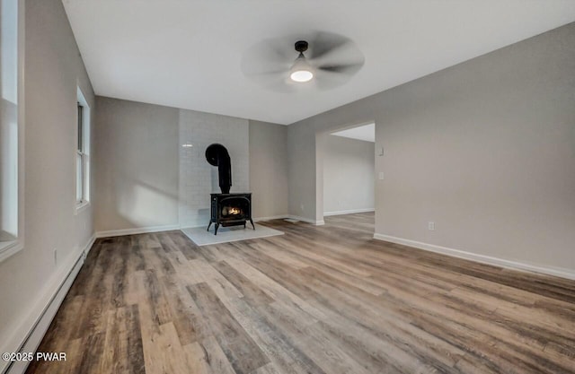 unfurnished living room featuring baseboard heating, ceiling fan, light hardwood / wood-style floors, and a wood stove