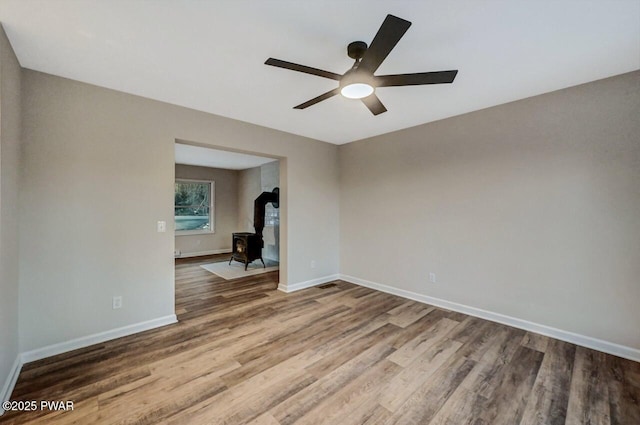 empty room with ceiling fan, hardwood / wood-style floors, and a wood stove