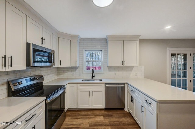 kitchen with sink, appliances with stainless steel finishes, tasteful backsplash, white cabinets, and kitchen peninsula