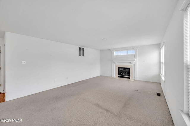 unfurnished living room featuring visible vents, a glass covered fireplace, and carpet floors