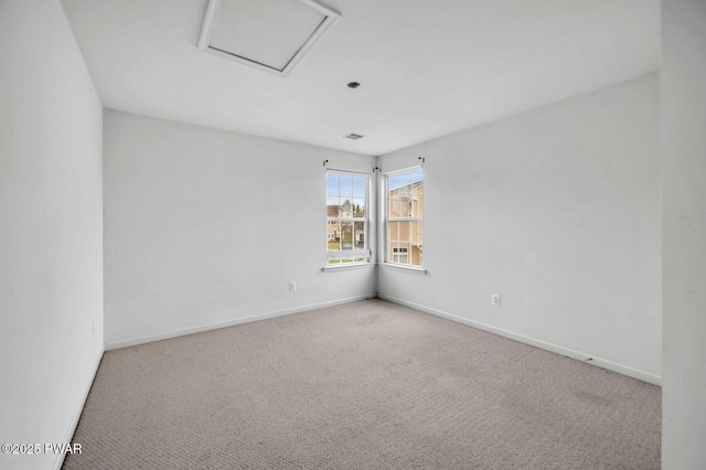 carpeted spare room featuring attic access and baseboards
