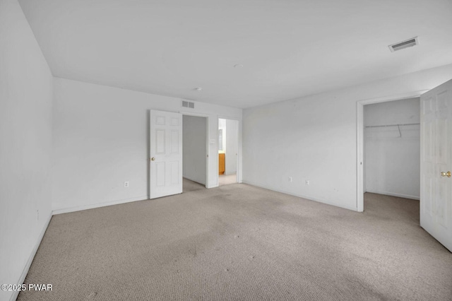 unfurnished bedroom with a walk in closet, carpet flooring, and visible vents