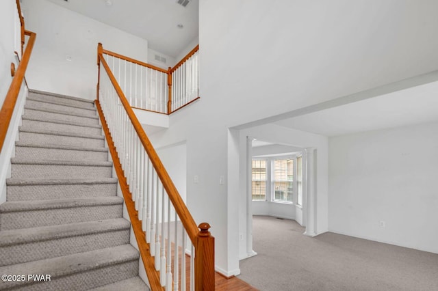staircase with carpet flooring, a towering ceiling, and visible vents