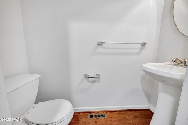 half bathroom featuring baseboards, toilet, visible vents, a sink, and wood finished floors