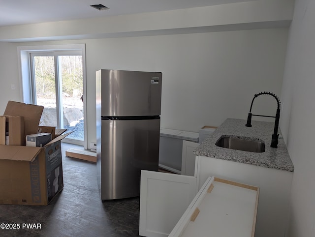 kitchen with white cabinets, stainless steel fridge, light stone counters, and sink