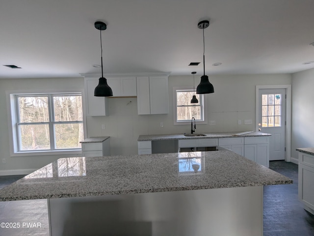 kitchen with white cabinets, a center island, light stone counters, and sink