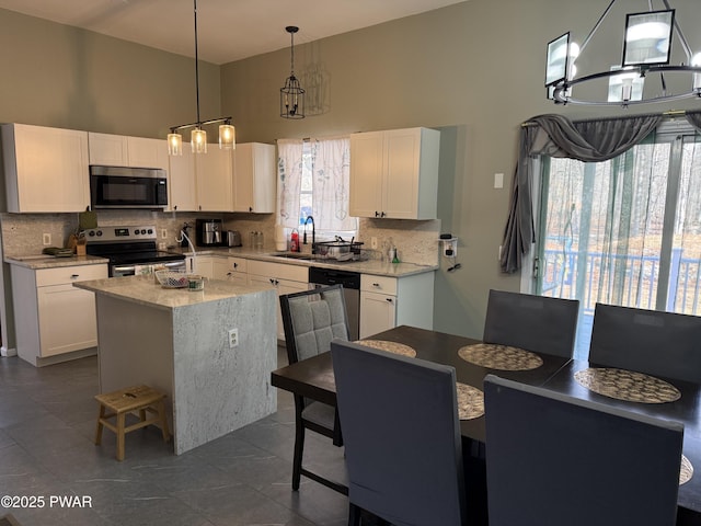 kitchen with appliances with stainless steel finishes, a center island with sink, white cabinets, and decorative light fixtures