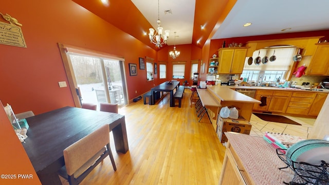 kitchen featuring lofted ceiling, decorative light fixtures, an inviting chandelier, kitchen peninsula, and light wood-type flooring