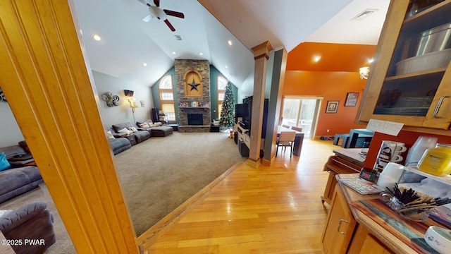 living room with a fireplace, ceiling fan, light wood-type flooring, high vaulted ceiling, and decorative columns