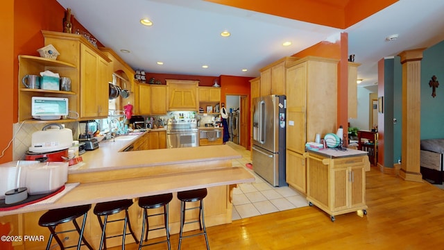 kitchen with appliances with stainless steel finishes, light hardwood / wood-style floors, kitchen peninsula, and a breakfast bar