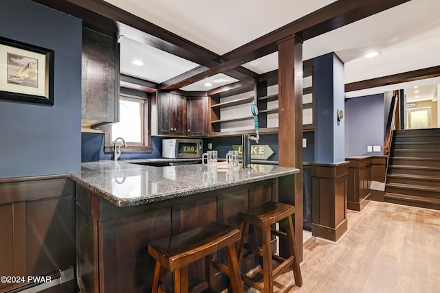 kitchen featuring beam ceiling, coffered ceiling, kitchen peninsula, dark stone counters, and light hardwood / wood-style floors