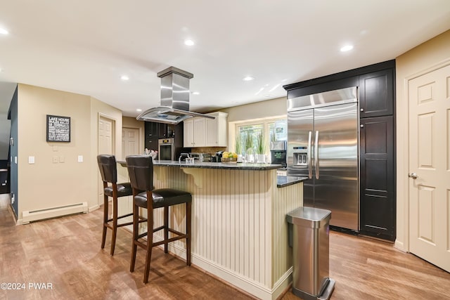 kitchen featuring a center island, a kitchen breakfast bar, built in refrigerator, baseboard heating, and island range hood