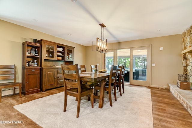 dining area featuring a baseboard heating unit, a stone fireplace, light hardwood / wood-style flooring, and a chandelier